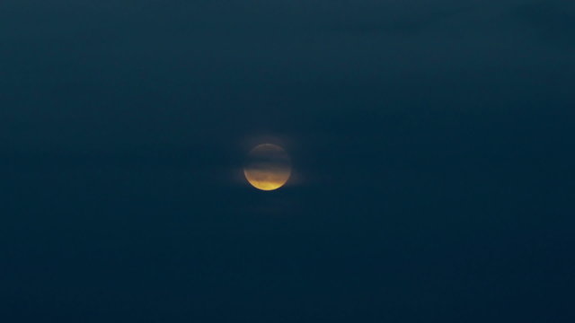 Timelapse full moon over late evening sky.