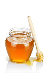 Glass jar of honey with wooden drizzler on a white background.