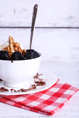 Dessert with prunes and nuts in cup on color wooden background
