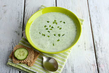 Cucumber soup in bowl on color wooden table background
