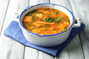 Carrot soup in bowl, on color wooden background