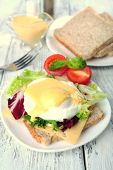 Toast with egg Benedict and tomato on plate on wooden table