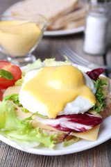 Toast with egg Benedict and tomato on plate on wooden table