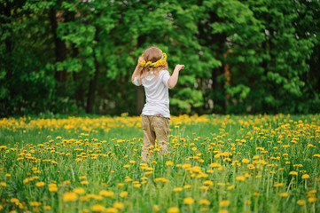 child girl in wreath walks on spring dandelion field