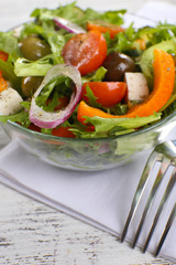 Greek salad in glass dish on napkin and color wooden background