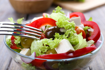 Greek salad in glass dish with fork on wooden table background