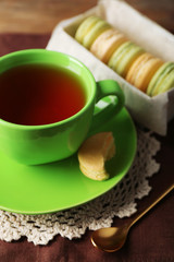 Colorful macaroons with cup of tea on wooden background