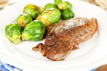 Roasted meat and vegetables on plate, on wooden table