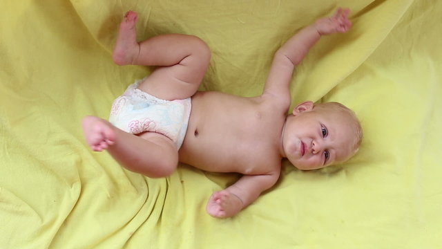 small blonde baby girl lay on yellow bed and jerk feet	