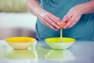 Female hands separating yolk and white of a cracked egg