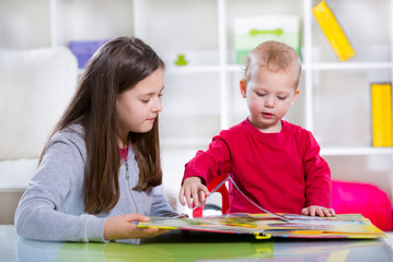 Two smiling children reading the book on the desk