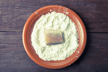 One piece of fresh fish with flour on a plate on a wooden backgr