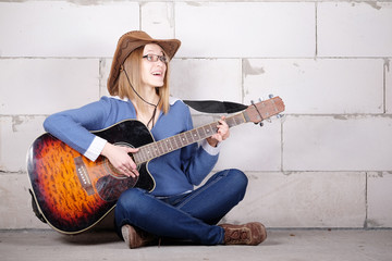 woman in a hat plays guitar sitting on the floor