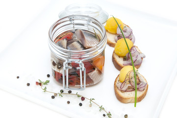 pickled herring in a glass jar with potato canapes