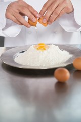 Close up of baker breaking eggs into flour