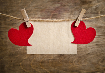 Red fabric hearts with sheet of paper hanging on the clothesline