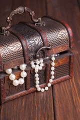 old treasure chest with pearl necklaces standing on wooden table