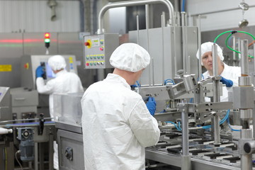 Naklejka premium three workers in uniforms at production line in plant