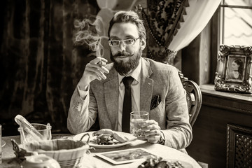 Man with a beard and mustache, smoking a cigar during dinner