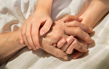 Fototapeta na wymiar hands of grandmother and grandchild in the bed