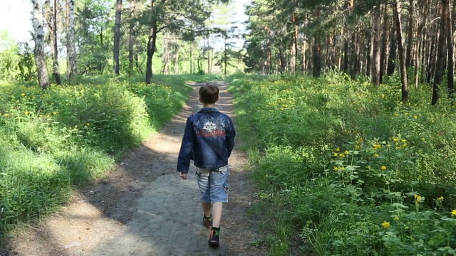 The boy is walking alone in the woods, shooting from behind