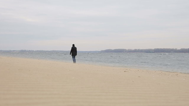 Sad pensive man walks along the sandy  shore, wide plan