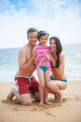 A couple at the beach posing in swimsuits with their daughter 
