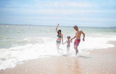 A young girl is running with her parents in the sea waves
