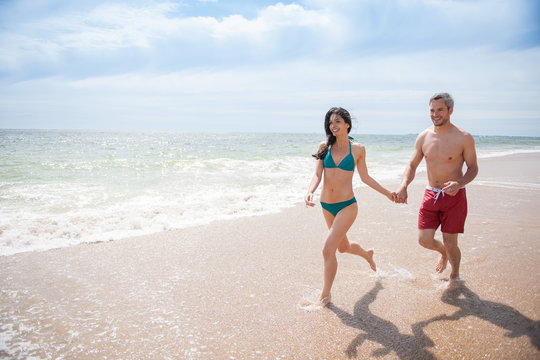 A young couple runs in the sea waves in swimsuit