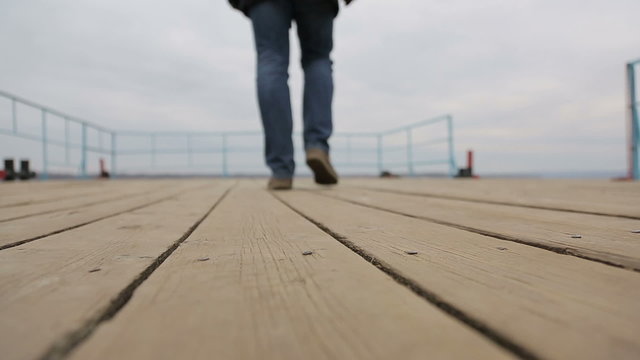 Sad pensive man walks on the pier, bottom view