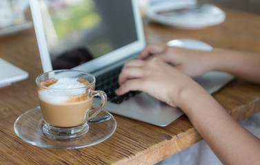 Closeup of coffee and hand typing on laptop keyboard