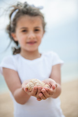 A dressed six year old is holding some seashells in her hands at