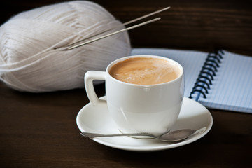 Cup of coffee with milk , warm woollen yarm on wooden backgraund