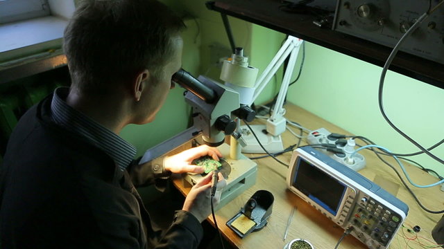 Scientist in the laboratory looking into a microscope and solder