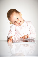 Cute little and smiling girl plays with a tablet