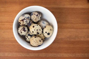 Quail eggs in white bowl on wooden table
