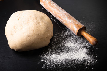 Dough, rolling pin and flour on a black background