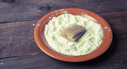 One piece of fresh fish with flour on a plate on a wooden backgr