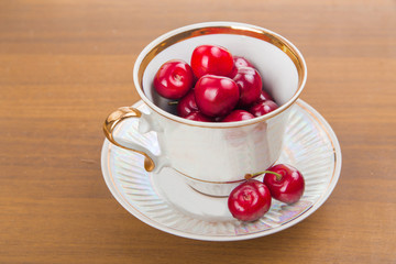 Sweet cherries in a white cup on a wooden table with two cherrie