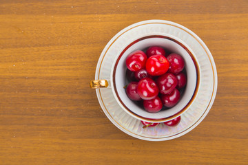 Sweet cherries in a white cup on a wooden table with two cherrie