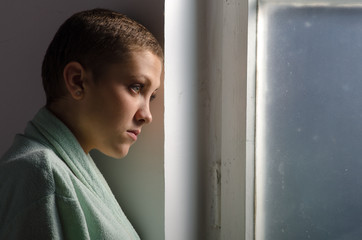 Young cancer patient standing in front of hospital window