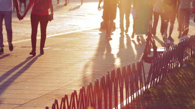 people walking at sunset on the sidewalk in a city, long shadows of people
