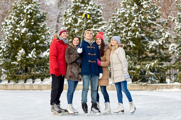 happy friends with smartphone on ice skating rink