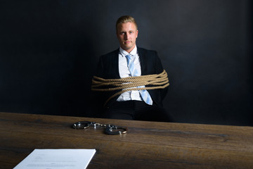 Businessman Tied With Rope Sitting In Front Of Table