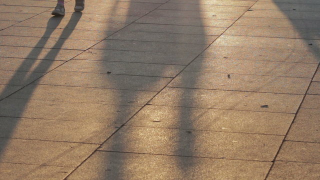 long shadows of people walking on the sidewalk at sunset