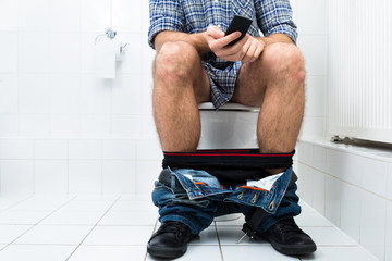 Man In Toilet Using Cellphone - obrazy, fototapety, plakaty