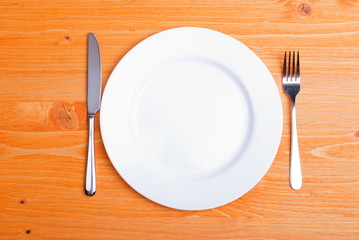 white plate and fork next to a knife on a wooden board top view