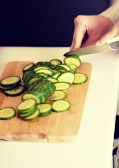 Woman cutting cucumber on kitchen board.