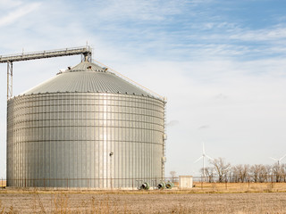 Grain bin with wind turbines in the background on a farm