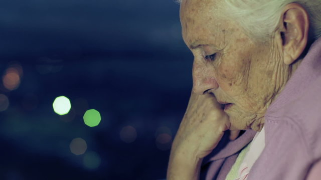 Pensive And Depressed  Old Woman Looking Out Window In The Night 